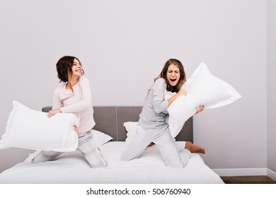 Two pretty girls having pajamas party. They fighting with pillow fight on bed - Powered by Shutterstock