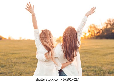 Two pretty girls raised their hands on a field at sunset.