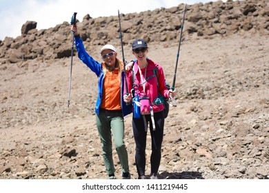 Two Pretty Girls In Sport Wear Standing On The Mountain With All Equipment For The Climbing. Rocks, No Plants And Trees. Dangerous And Extreme Adventure In Africa. Comfortable Shoes, Holding Sticks