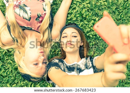 Two pretty girls taking a self portrait - Young women with a sportive casual outfit lying on meadow and having fun while taking a selfie