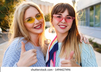 Two Pretty Happy Couple Of Woman Showing Thumbs Up Sign , Smiling And Having Fun , Trendy Elegant Pastel Clothes And Vintage Glasses, Soft Colors And Matching Outfits, Sister Best Friends .