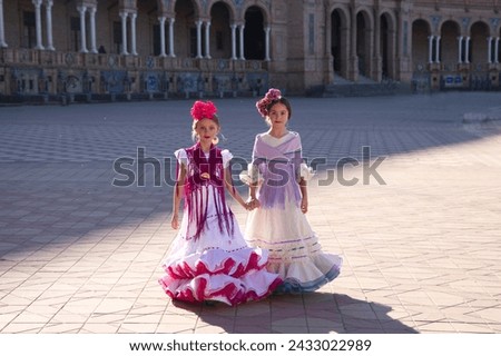 Two pretty little girls dancing flamenco dressed in typical gypsy costumes walk hand in hand through a famous square in Seville. The girls are happy. Flamenco, cultural heritage of humanity