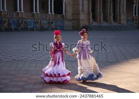 Two pretty little girls dancing flamenco dressed in typical gypsy costumes walk hand in hand through a famous square in Seville. The girls are happy. Flamenco, cultural heritage of humanity