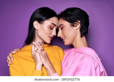 Two pretty sexy stylish cool generation z girls lgbtq lesbian couple dating in love hugging enjoying intimate tender sensual moment together holding hands isolated on purple background. Close up view