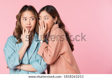 Two pretty women whispering in ear a secret story. Portrait isolated on pink studio background. 