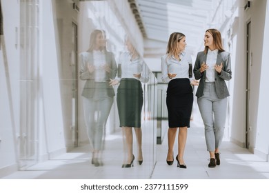 Two pretty young business women walking and discussing in the office hallway