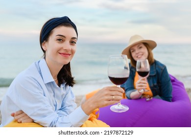 Two Pretty Young Women With Glasses Of Red Wine By The Sea. Sunset, Evening Sky.