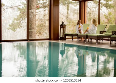 Two Pretty Young Women Relaxing On The Deckchair By The Swimming Pool In Spa