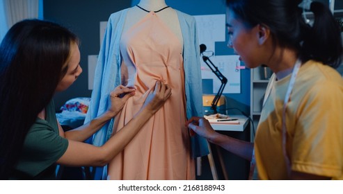 Two professional Asia cheerful lady fashion designer teamwork with casual overtime work share idea create beautiful dress on dummy in shop at night. Lady tailor business partner start up business. - Powered by Shutterstock