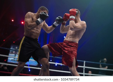 Two professional boxers in dynamic boxing action on the ring under lights of sport arena soffits. Boxer hit opponent