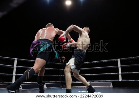 Two professional boxers in dynamic boxing action in the ring under the lights of a sporting arena. Opponent hit sportsmen at the match 