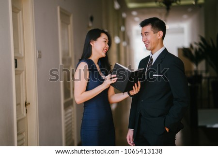 Two professional Chinese Asian lawyers (a man in a suit and woman in a dress) have a discussion while looking over a notebook.