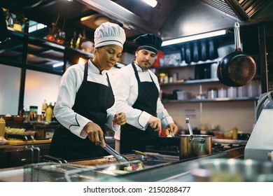 Two professional cooks preparing meal in the kitchen at restaurant. Focus is on African American female chef.