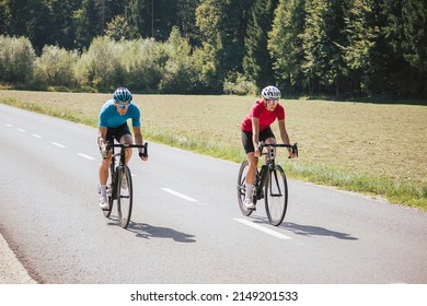 Two Professional Cyclist Racers, Male And Female During Training On A Paved Road Through The Mountain Landscape, Front View.