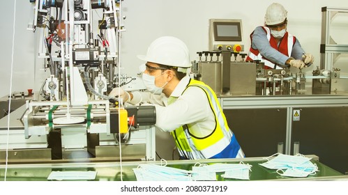 Two Professional Electrical Engineers Wearing Masks And Safety Helmets To Troubleshoot The Electrical Control System Of The Mask Maker Are Helping To Inspect The Automatic Conveyor Belt For Safety.