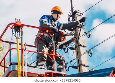 Two professional electricians in hard hats are repairing power lines from cradle of bucket truck. View from below. Electricians change cables on street lighting poles.