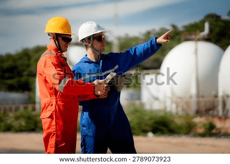 two professional engineer, worker, technician use clipboard discuss work, discussing operations at a gas storage facility. protective uniforms and helmets. industry, engineer, safety, teamwork, energy