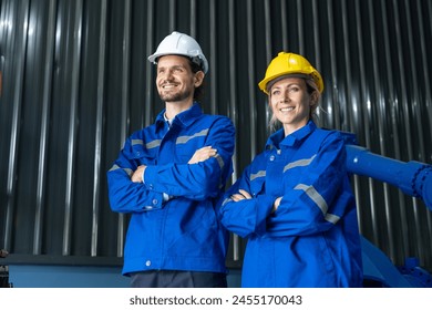 Two professional engineers in hard hats and blue workwear standing confidently in an industrial facility with arms crossed. - Powered by Shutterstock