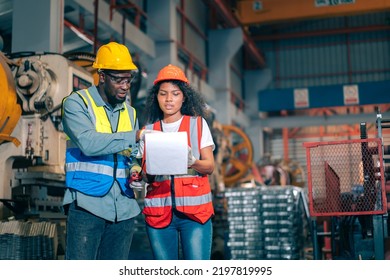 Two Professional Engineer,worker,technician Use Clipboard Discuss Work, Walk In Steel Metal Manufacture Factory Plant Industry. Black African American Man And Woman Wear Hard Hat Check Quality Machine