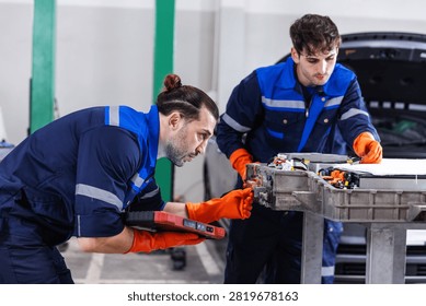 Two professional EV technicians performing a detailed inspection of high-voltage battery connectors during electric vehicle maintenance in a modern service workshop. 