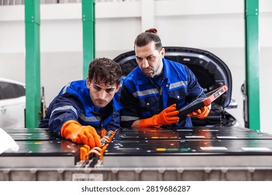 Two professional EV technicians performing a detailed inspection of a high-voltage battery pack in a modern electric vehicle service workshop. 
