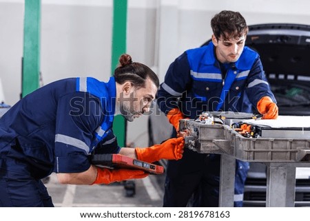 Two professional EV technicians performing a detailed inspection of high-voltage battery connectors during electric vehicle maintenance in a modern service workshop. 