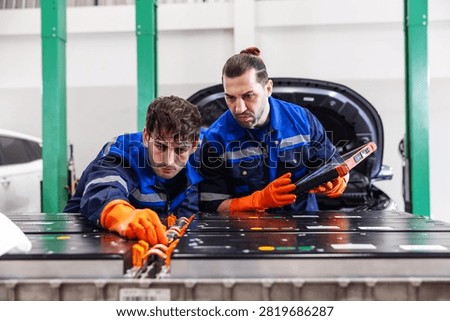 Two professional EV technicians performing a detailed inspection of a high-voltage battery pack in a modern electric vehicle service workshop. 
