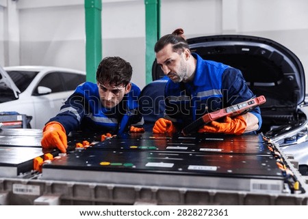 Two professional EV technicians performing a detailed inspection of a high-voltage battery pack in a modern electric vehicle service workshop. 