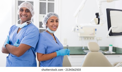 Two professional hispanic dentists in blue uniforms standing back to back in modern office of dental clinic - Powered by Shutterstock