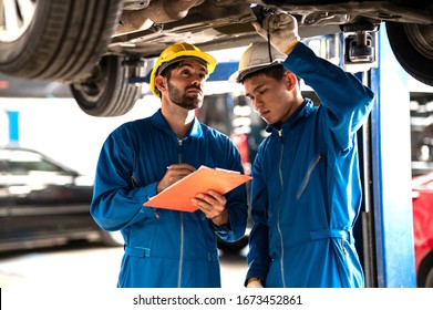 Two professional look technician inspecting car underbody and suspension system by using check list in moder car service shop. Automotive business or car repair concept.