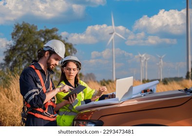 Two professional maintenance engineers in safety workwear using laptop and tablet checklist wind turbine on windmill construction farms. Sustainable renewable energy and clean environment concept. - Powered by Shutterstock