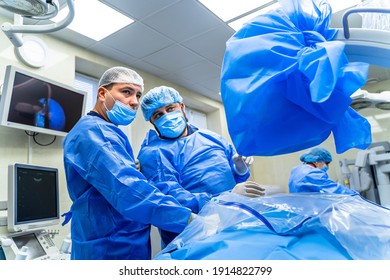 Two Professional Medics Look At The Screen While Providing Complex Neurosurgery Operation. Blue Tones In Operation Room.