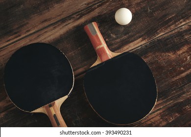 Two professional ping pong rockets lying on vintage wooden table. Black antispin pads. One attack plus, other defense, japan and german made. White ball is near.