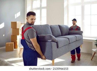 Two professional relocation service workers in overalls move sofa in customer's apartment. Movers carry sofa, cardboard boxes and assembling furniture. Moving and delivery company services. - Shutterstock ID 2135966153