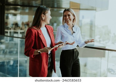 Two professional women engage in a thoughtful discussion while reviewing a tablet outside a sleek, contemporary office building during the daytime. - Powered by Shutterstock