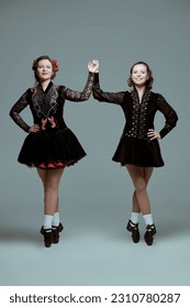 Two professional women's Irish dance ensemble in concert costumes and Ghillies Hard Shoes pose together in a row. Full-length studio portrait on a grey background. - Shutterstock ID 2310780287