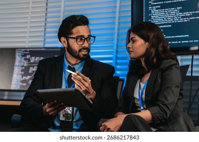 Two professionals analyze and discuss programming code displayed on screen in modern tech workspace. Capturing a collaborative environment focused on software development, debugging, and teamwork