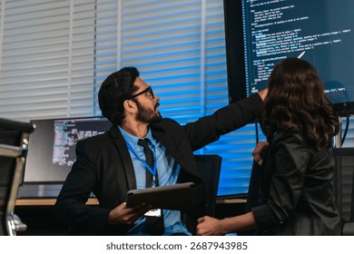 Two professionals analyze and discuss programming code displayed on screen in modern tech workspace. Capturing a collaborative environment focused on software development, debugging, and teamwork