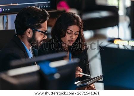 Two professionals analyze and discuss programming code displayed on screen in modern tech workspace. Capturing a collaborative environment focused on software development, debugging, and teamwork