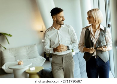 Two professionals chat and smile while walking through a stylish office. Natural light fills the space, creating an inviting atmosphere.