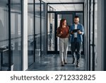 Two professionals collaborate while walking in a modern office setting, sharing ideas and using digital tools.