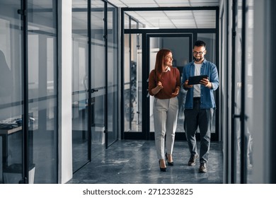 Two professionals collaborate while walking in a modern office setting, sharing ideas and using digital tools.