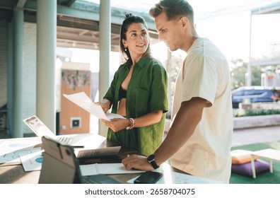Two professionals collaborating during remote workday, combining laptop use and printed data in an intuitive flow of digital communication and strategic planning.