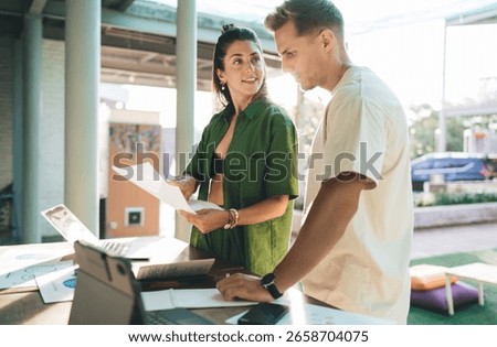 Two professionals collaborating during remote workday, combining laptop use and printed data in an intuitive flow of digital communication and strategic planning.