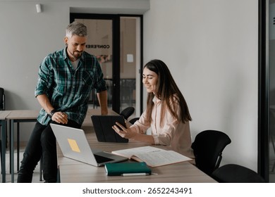 Two professionals collaborating in an office, using devices to discuss and share ideas.