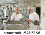 Two professionals in a commercial kitchen are using digital tablet while conducting a food safety inspection in well-equipped food processing facility