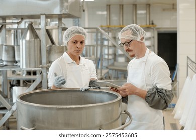 Two professionals in a commercial kitchen are using digital tablet while conducting a food safety inspection in well-equipped food processing facility