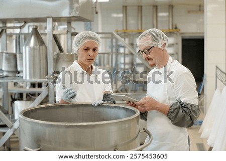 Two professionals in a commercial kitchen are using digital tablet while conducting a food safety inspection in well-equipped food processing facility