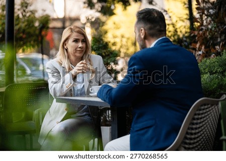 Two professionals discussing work topics at a street cafe. A businesswoman and a businessman networking outdoors