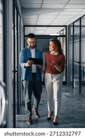 Two professionals discussing work while walking in an office hallway, fostering collaboration and teamwork.